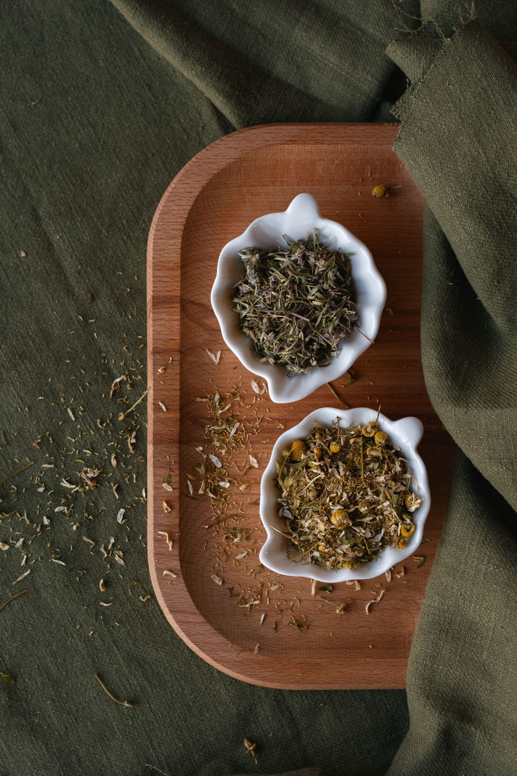 Dried chamomile and herbal tea blends in ceramic bowls on a wooden tray